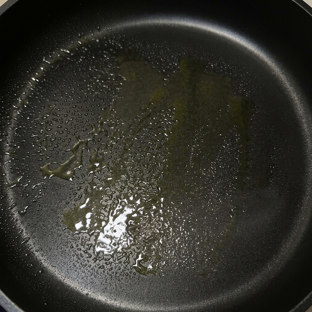 Una sartén negra con una capa brillante de mantequilla derretida y aceite de oliva lista para cocinar.