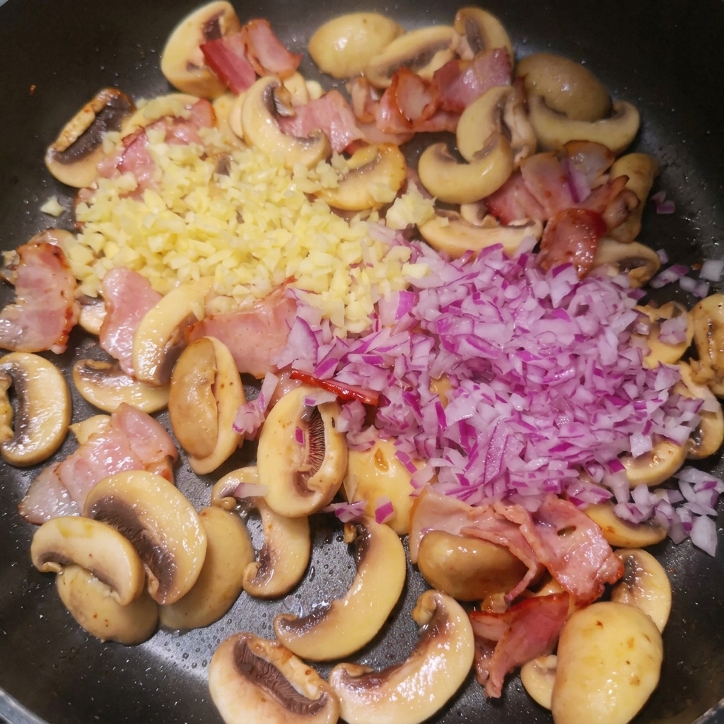 Cebolla roja y ajo picados sobre el bacón cocinado y los champiñones en la sartén.