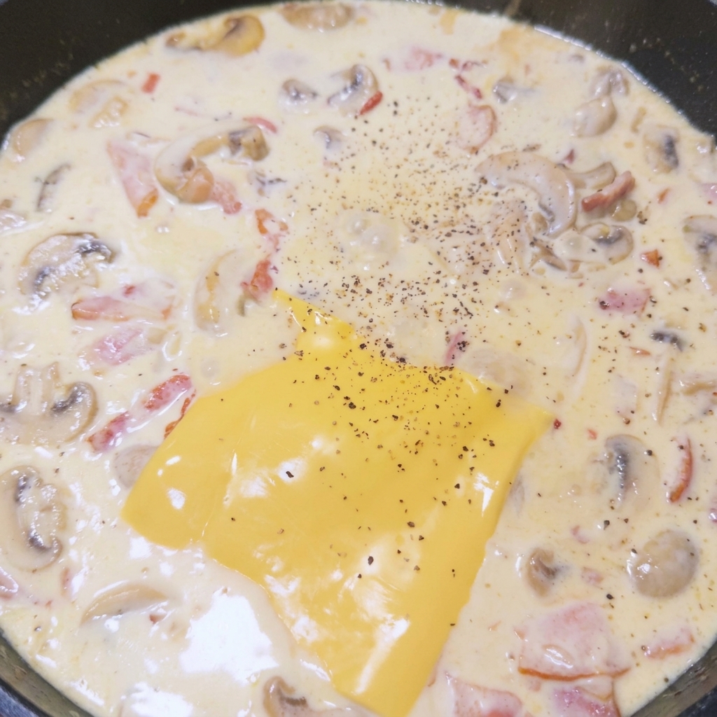 Loncha de queso fundiéndose en la salsa de crema, sazonada con pimienta negra recién molida.