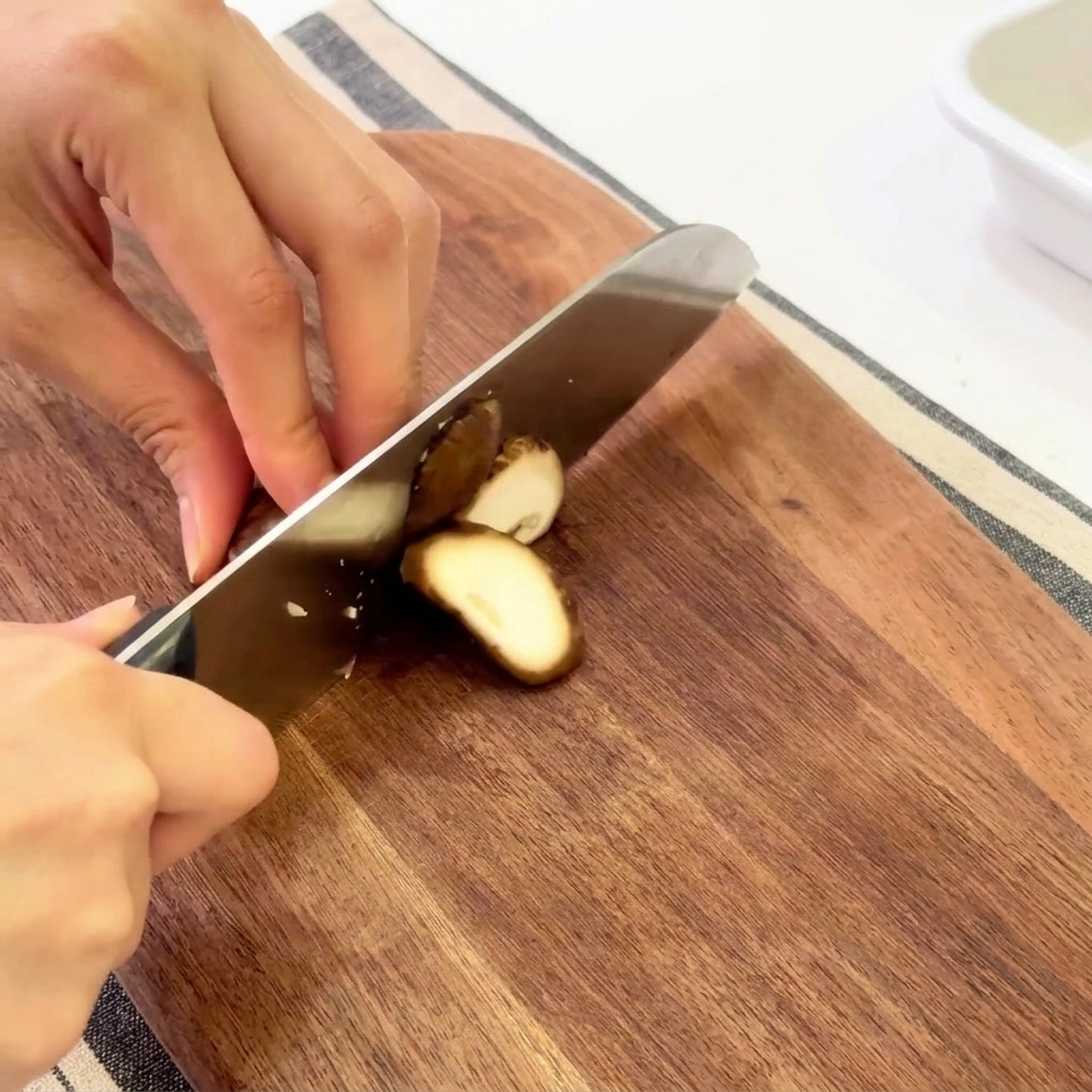 Manos laminando setas shiitake frescas sobre una tabla de cortar de madera.