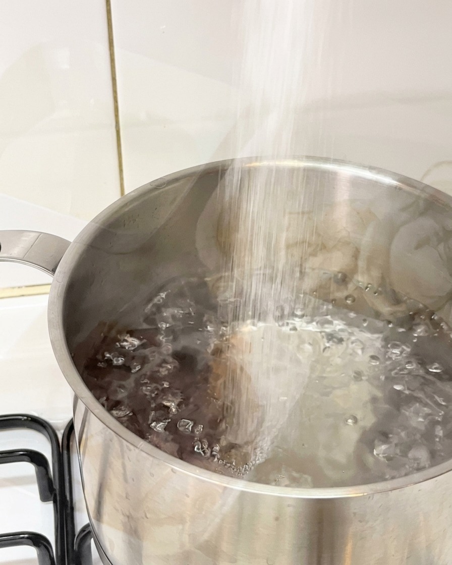 Sal vertiéndose en una olla de acero inoxidable con agua hirviendo vigorosamente.