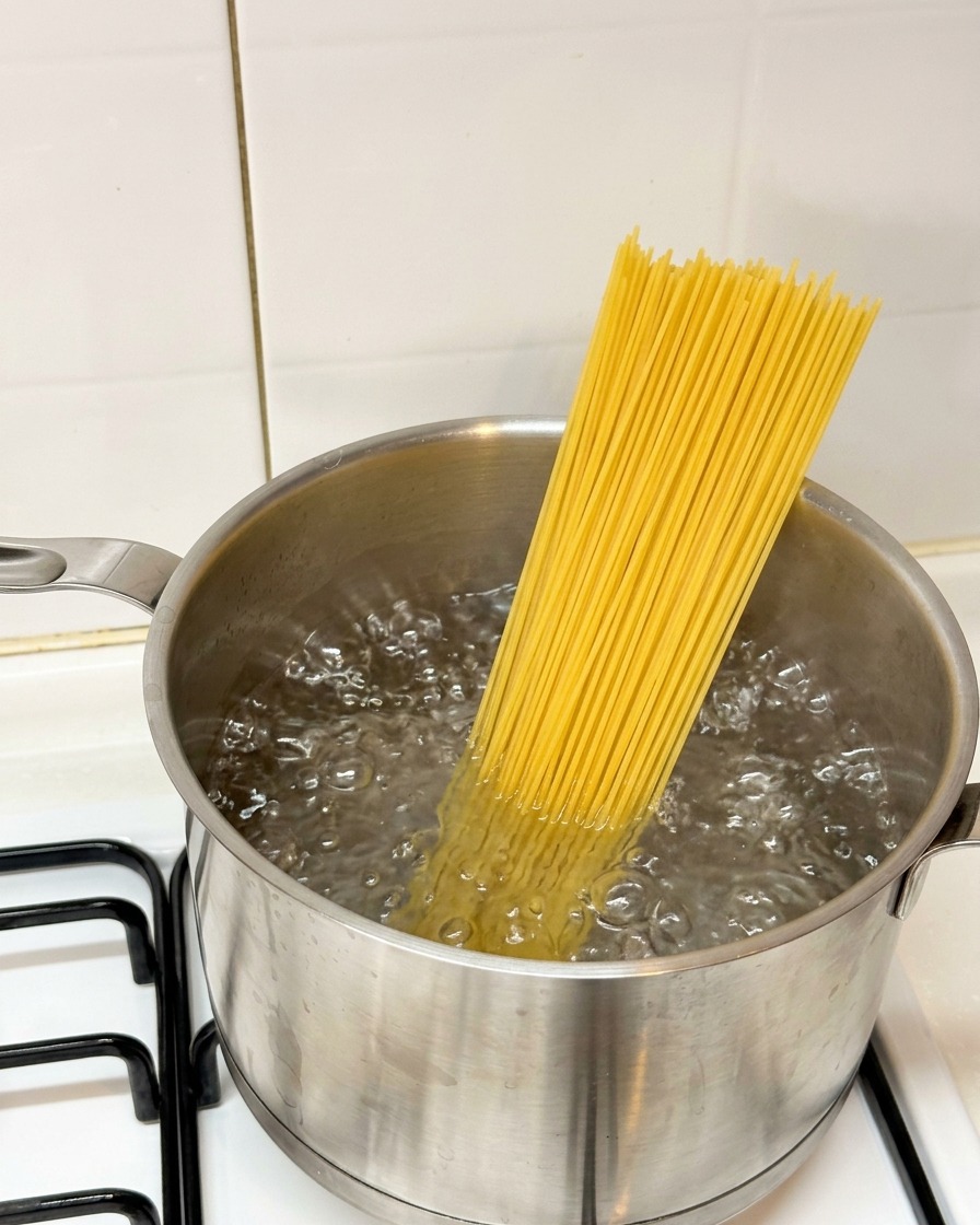 Espaguetis secos introduciéndose en una olla con agua hirviendo sobre el fuego.