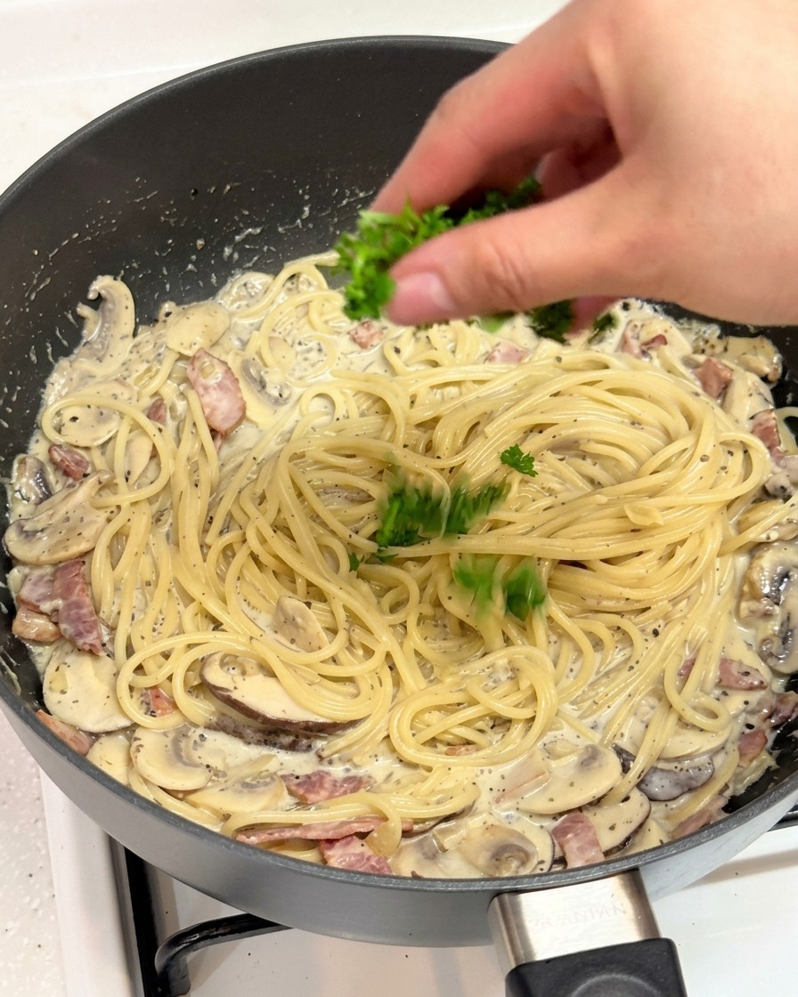 Una mano espolvoreando perejil verde fresco picado sobre una sartén de pasta cremosa a la trufa.