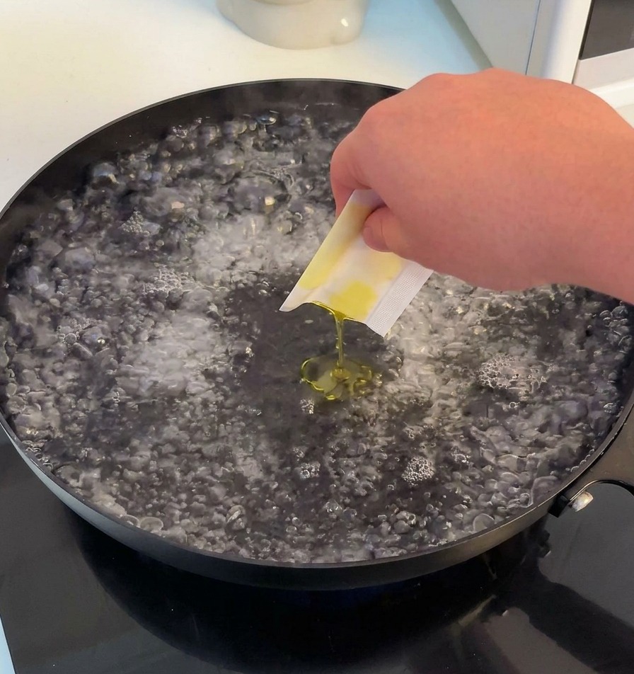 Una mano vertiendo sal y aceite de oliva en una olla con agua hirviendo.