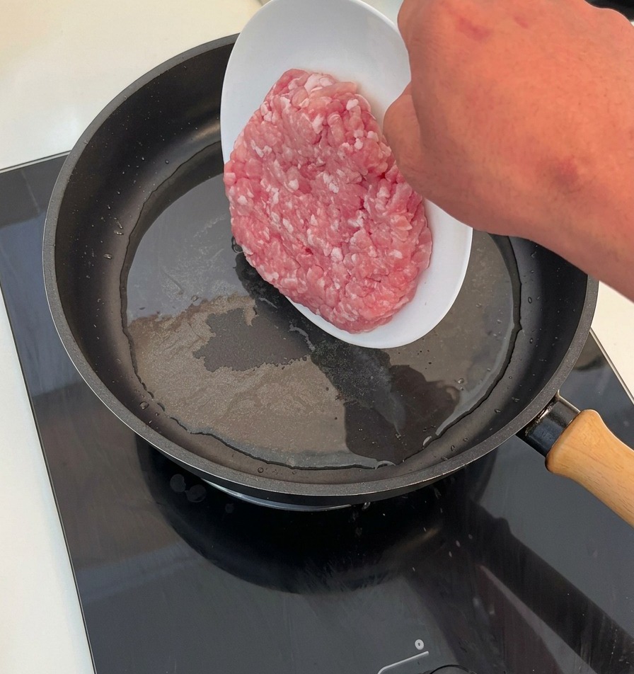 Carne picada cruda deslizándose desde un plato hacia una sartén caliente con aceite.