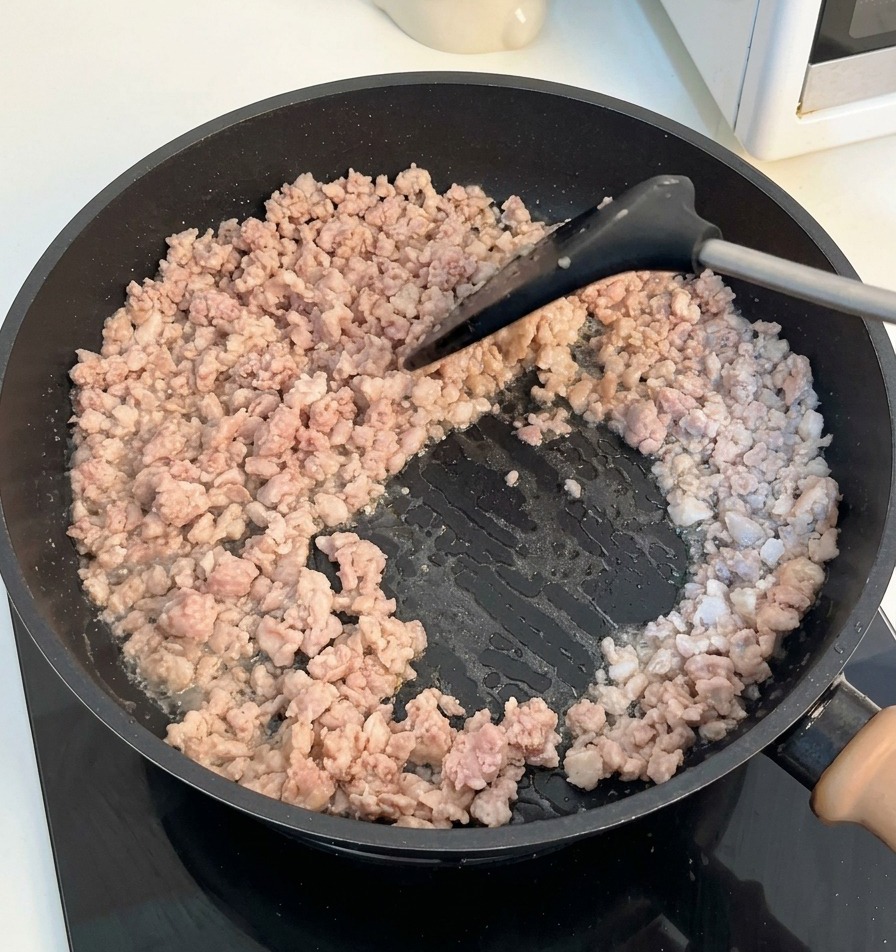 Una espátula removiendo y desmenuzando la carne picada dorada en una sartén.