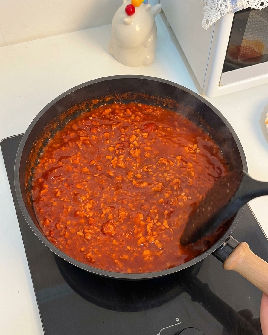 Salsa de tomate y carne burbujeando intensamente en una sartén mientras se remueve.