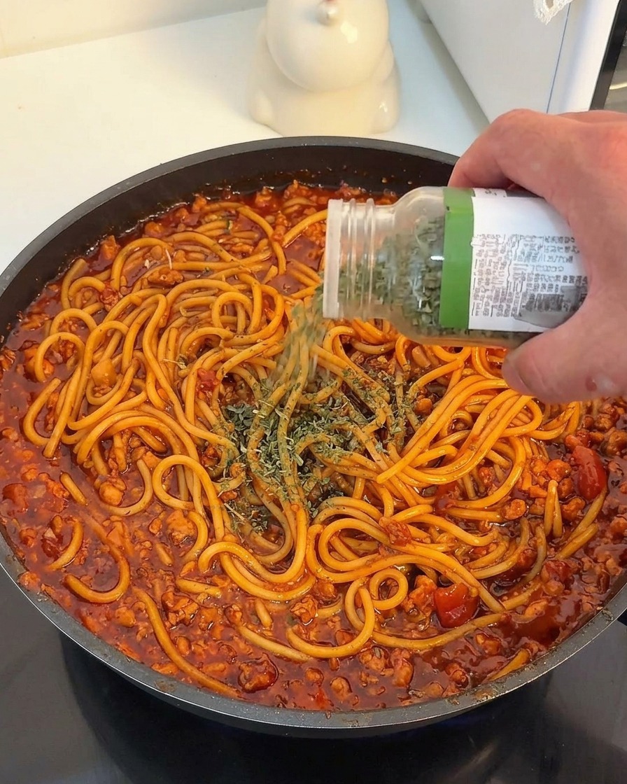 Una mano espolvoreando perejil seco sobre los espaguetis con salsa roja de carne.