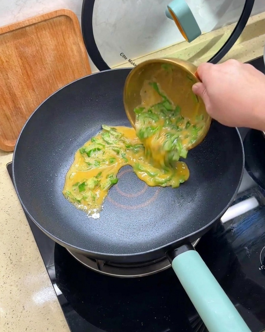 Vertiendo la mezcla de huevos batidos y lechuga picada desde un bol dorado a una sartén antiadherente caliente.
