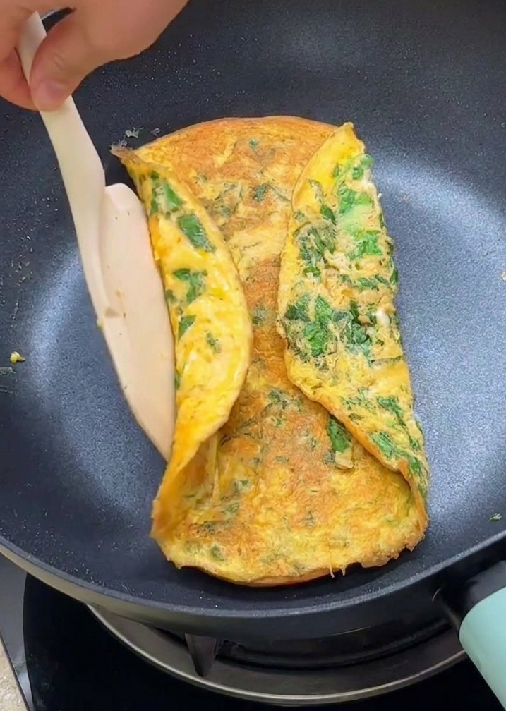 Una espátula doblando los bordes de la tortilla de lechuga sobre las mitades de pan tostado en la sartén.