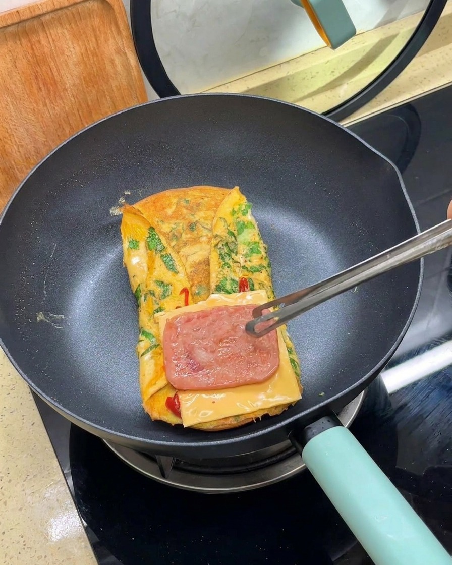 Unas pinzas colocando una loncha de carne cocinada sobre el queso en la tortilla dentro de la sartén.