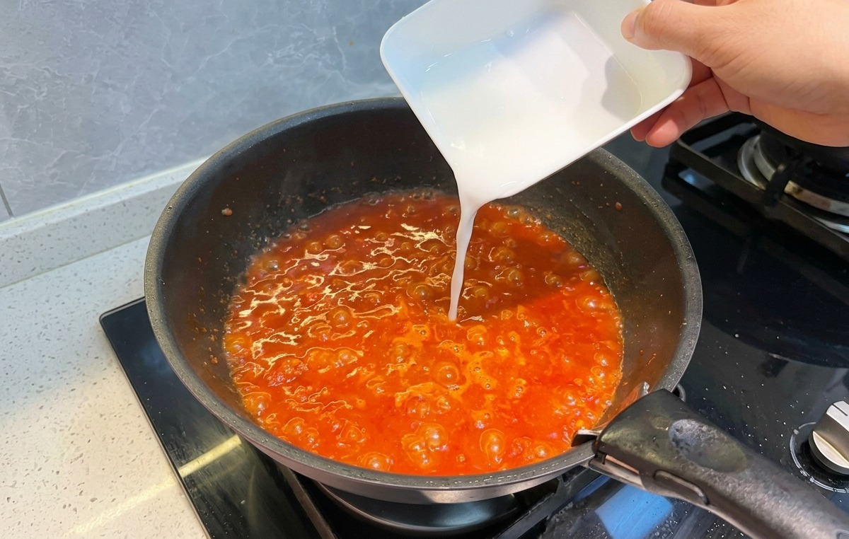 Vertiendo una mezcla blanquecina de almidón en la salsa de tomate burbujeante.