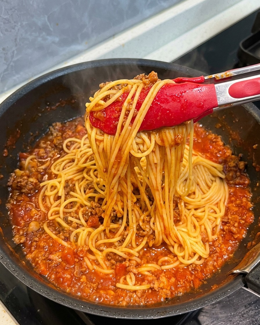 Pinzas rojas levantando espaguetis totalmente cubiertos por una rica salsa de carne.