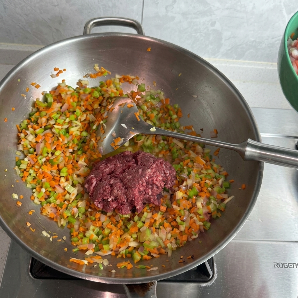 Carne picada de cerdo y ternera cruda sobre una cama de verduras salteadas en un wok de acero inoxidable.