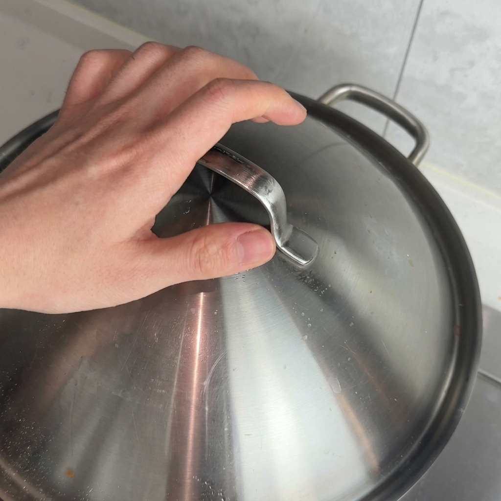 Una mano colocando una tapa de metal sobre una olla para que la salsa de carne repose al fuego.