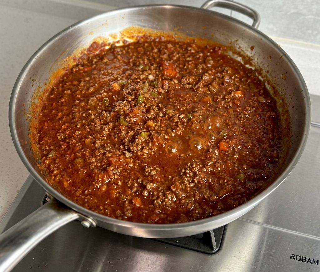 Salsa de carne roja, espesa y burbujeante cocinándose en una sartén de acero inoxidable.