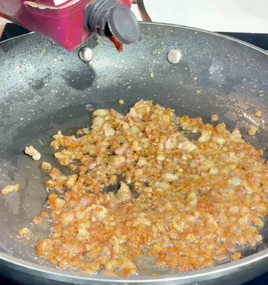 Vertiendo vino tinto desde un cartón pequeño en una sartén con carne de cerdo picada dorada.