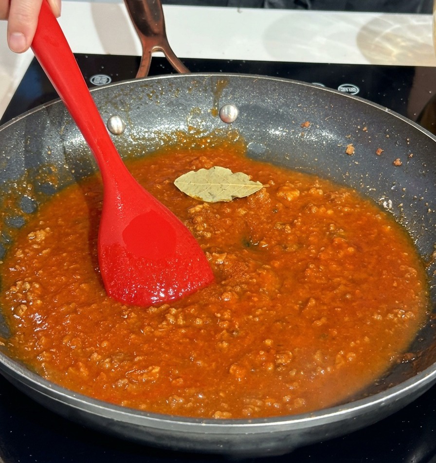 Una hoja de laurel seca sobre una rica salsa de carne roja en una sartén.