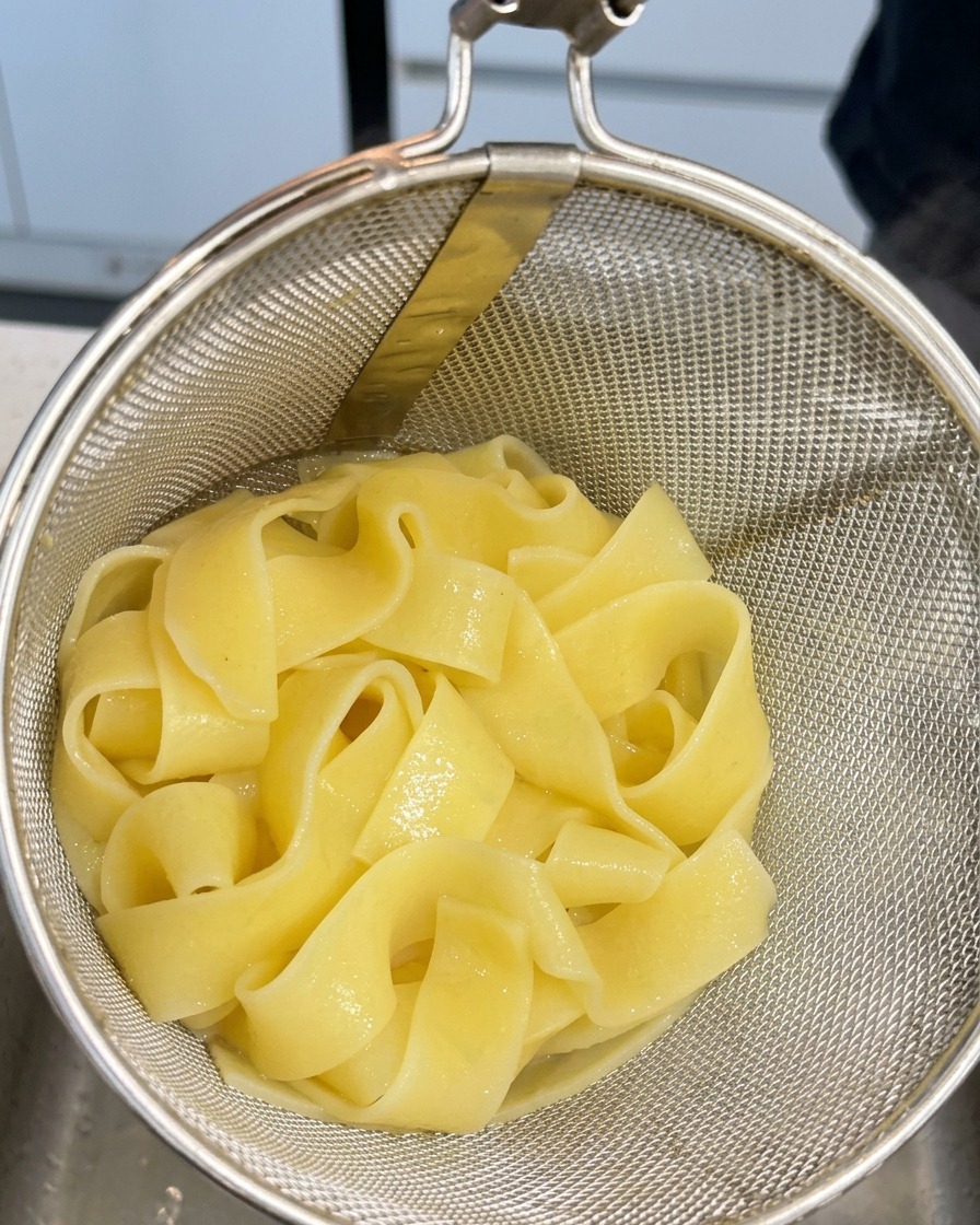 Pasta pappardelle cocida reposando en un colador metálico tras sacarla del agua hirviendo.