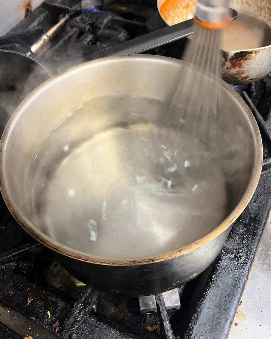 Batiendo agua hirviendo en una olla de metal para crear un remolino.