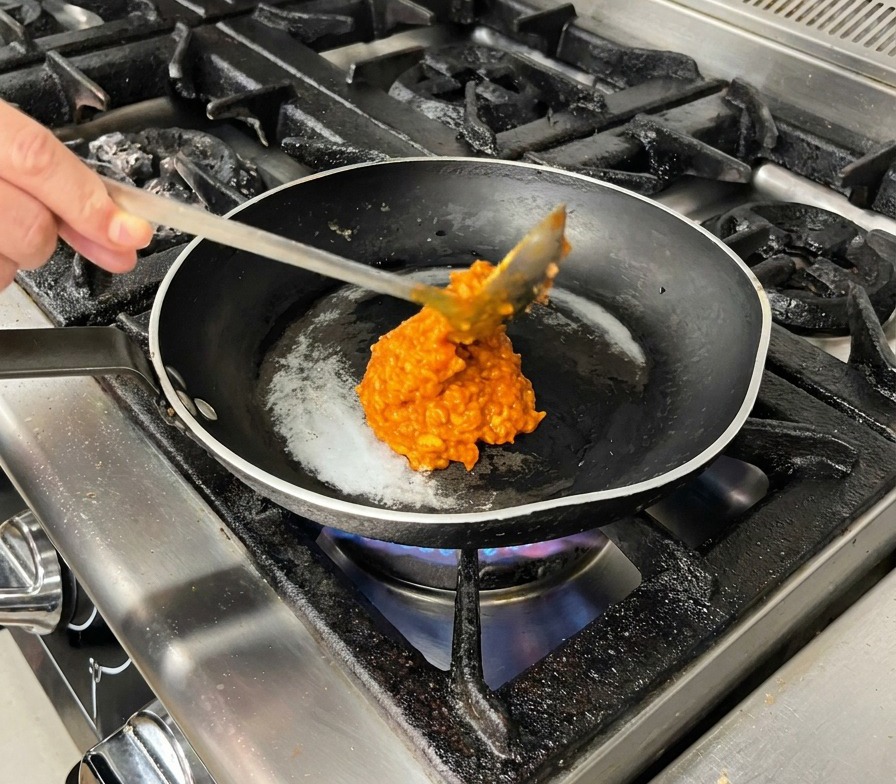 Una cucharada grande de salsa de carne roja espesa vertiéndose en una sartén negra caliente.