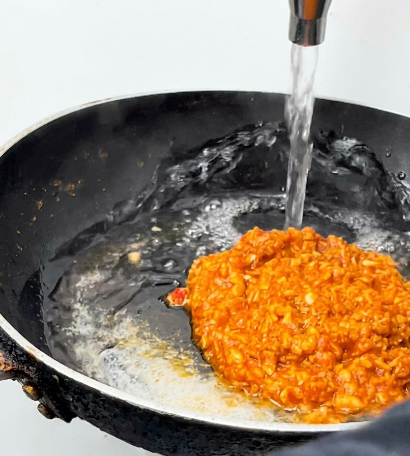 Un chorro de agua vertiéndose en una sartén con salsa de carne roja hirviendo.