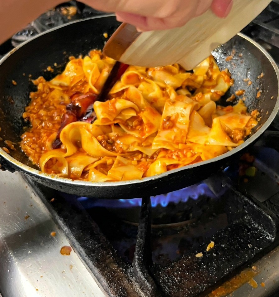 Vertiendo salsa oscura desde un plato pequeño sobre la pasta en la sartén.