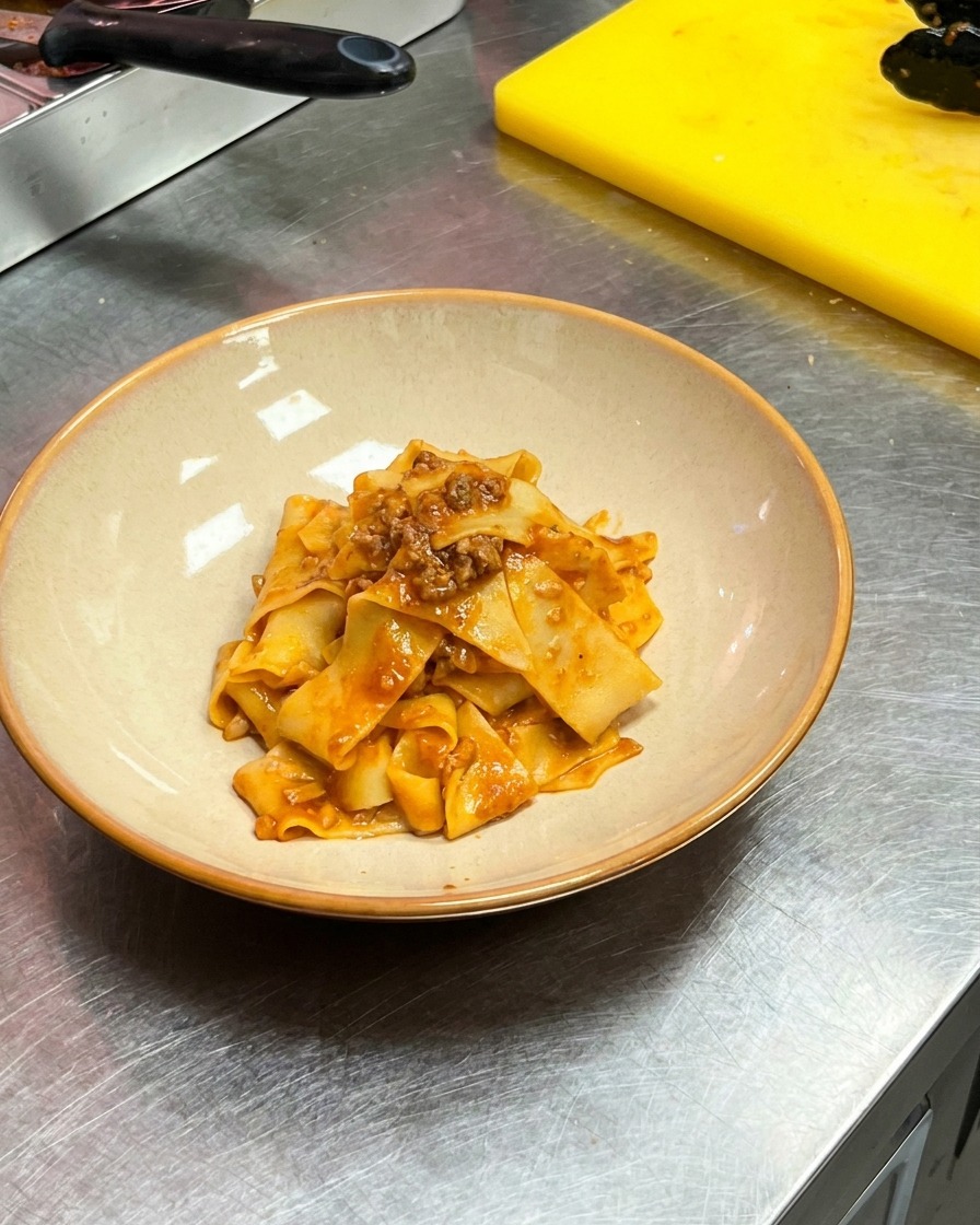 Pinzas pasando pappardelle con salsa a un bol de cerámica redondo.