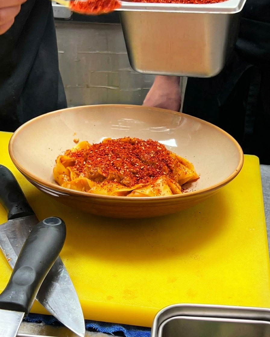 Una cucharada de copos de chile rojo vertiéndose en el centro de la pasta.