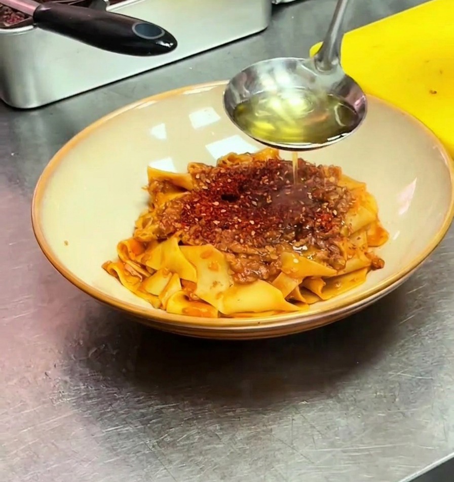 Un cucharón vertiendo aceite caliente sobre chile en polvo encima de la pasta.