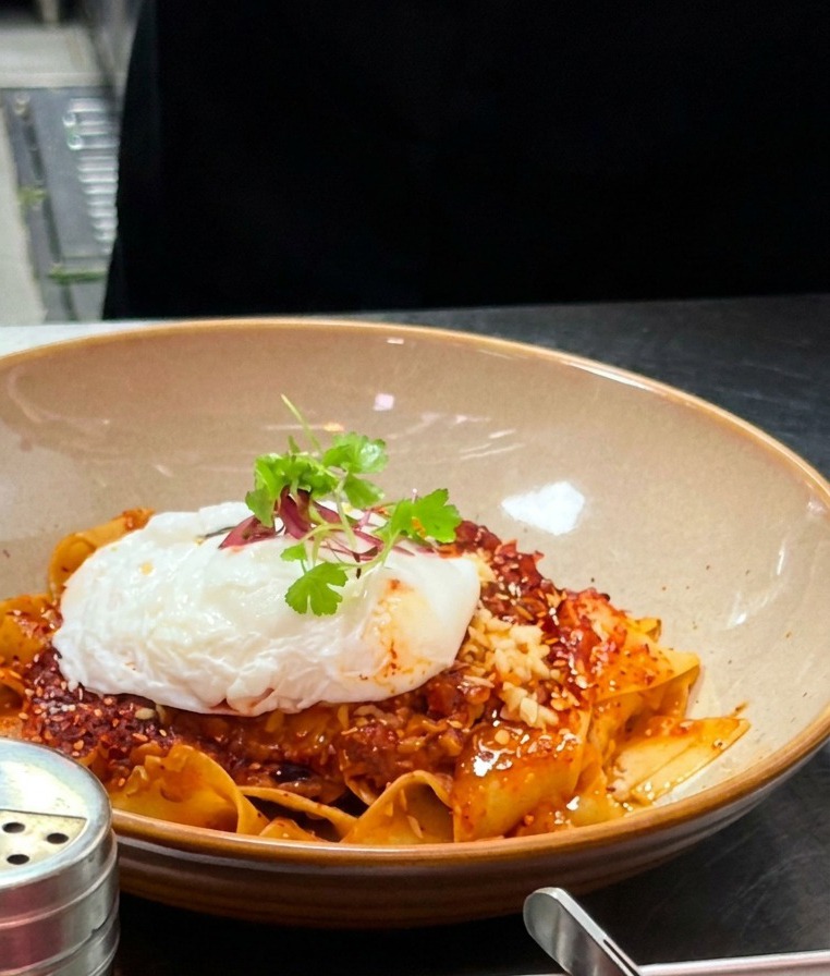 Un bol terminado de pappardelle con huevo poché, aceite de chile y microbrotes.