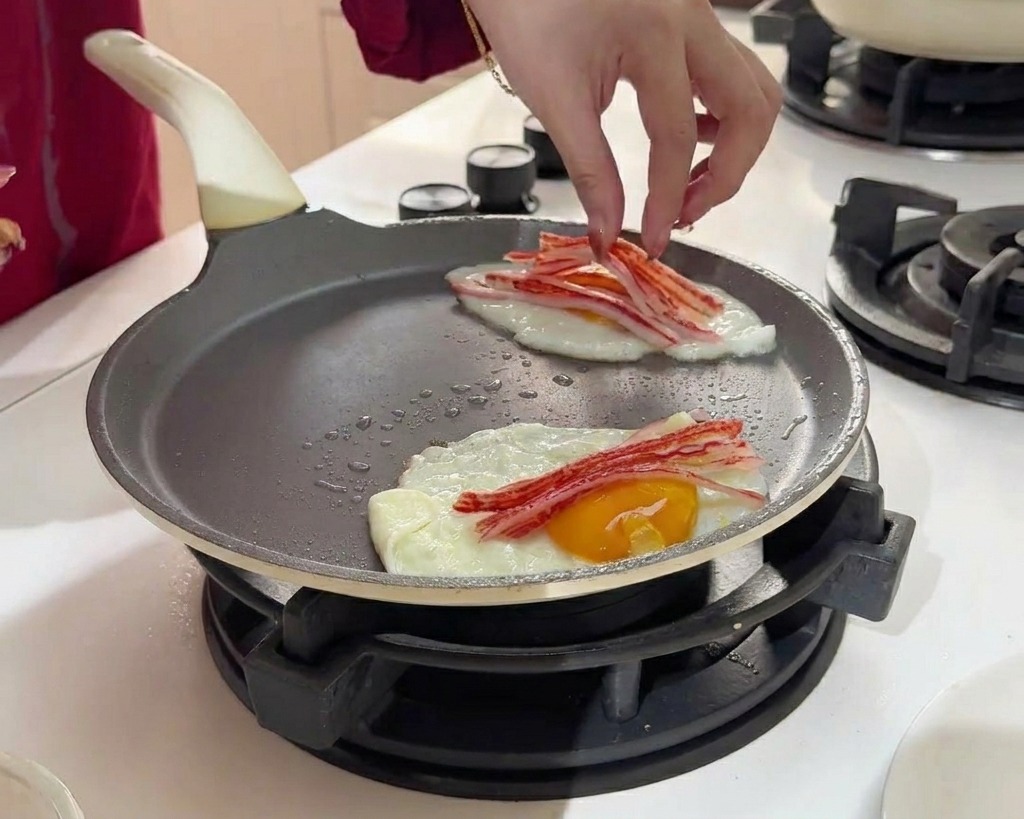 Colocando tiras finas de palitos de cangrejo rojos y blancos sobre la superficie de dos huevos friéndose.