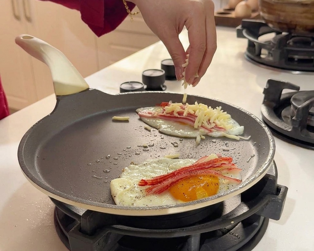 Una mano espolvoreando queso blanco rallado sobre los huevos y el cangrejo en la sartén.