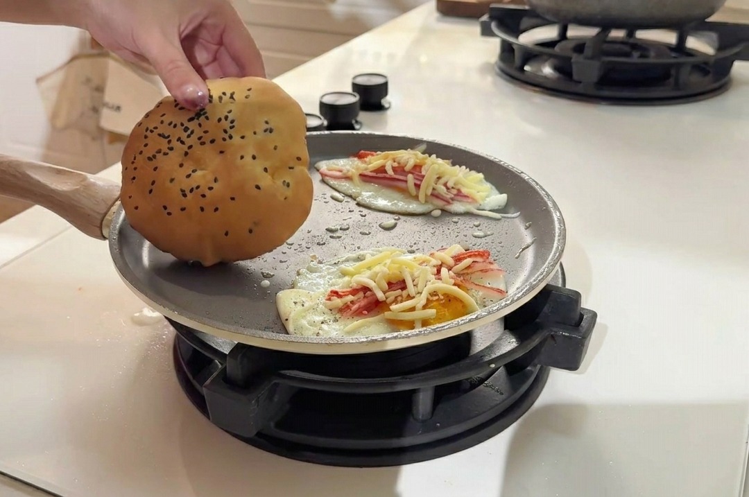Colocando un pan de hamburguesa con semillas de sésamo en la sartén junto a los huevos.