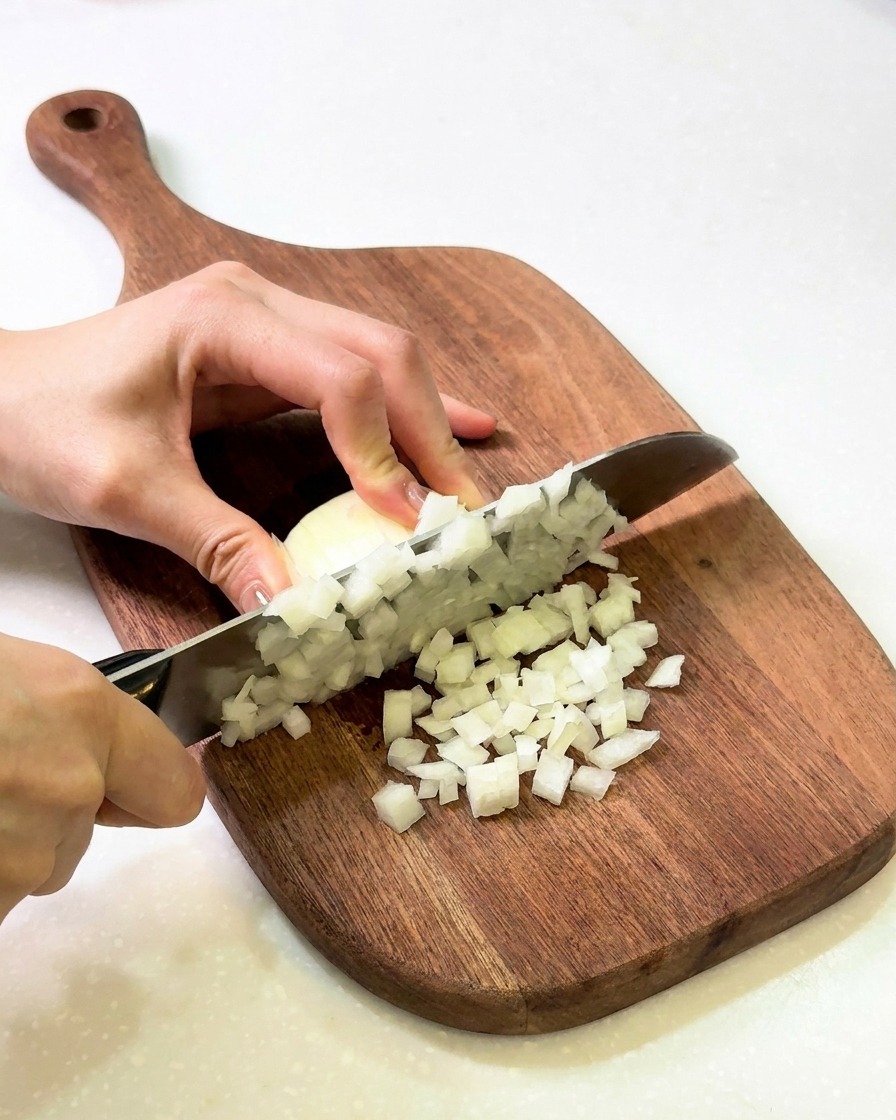 Picar una cebolla blanca en cubos pequeños sobre una tabla de madera.