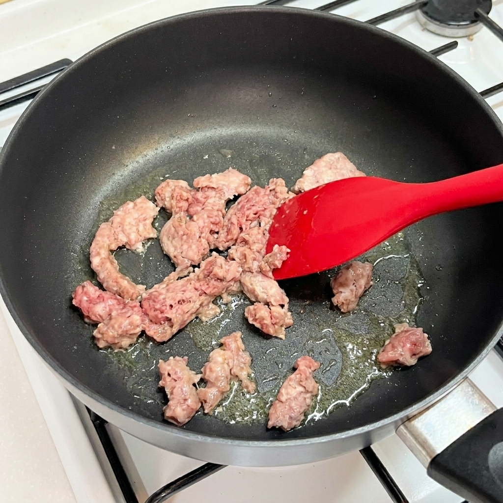 Carne picada de ternera dorándose en una sartén con una espátula de silicona.