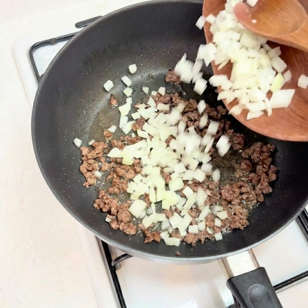 Cebolla picada añadiéndose a la carne de ternera dorada en una sartén.