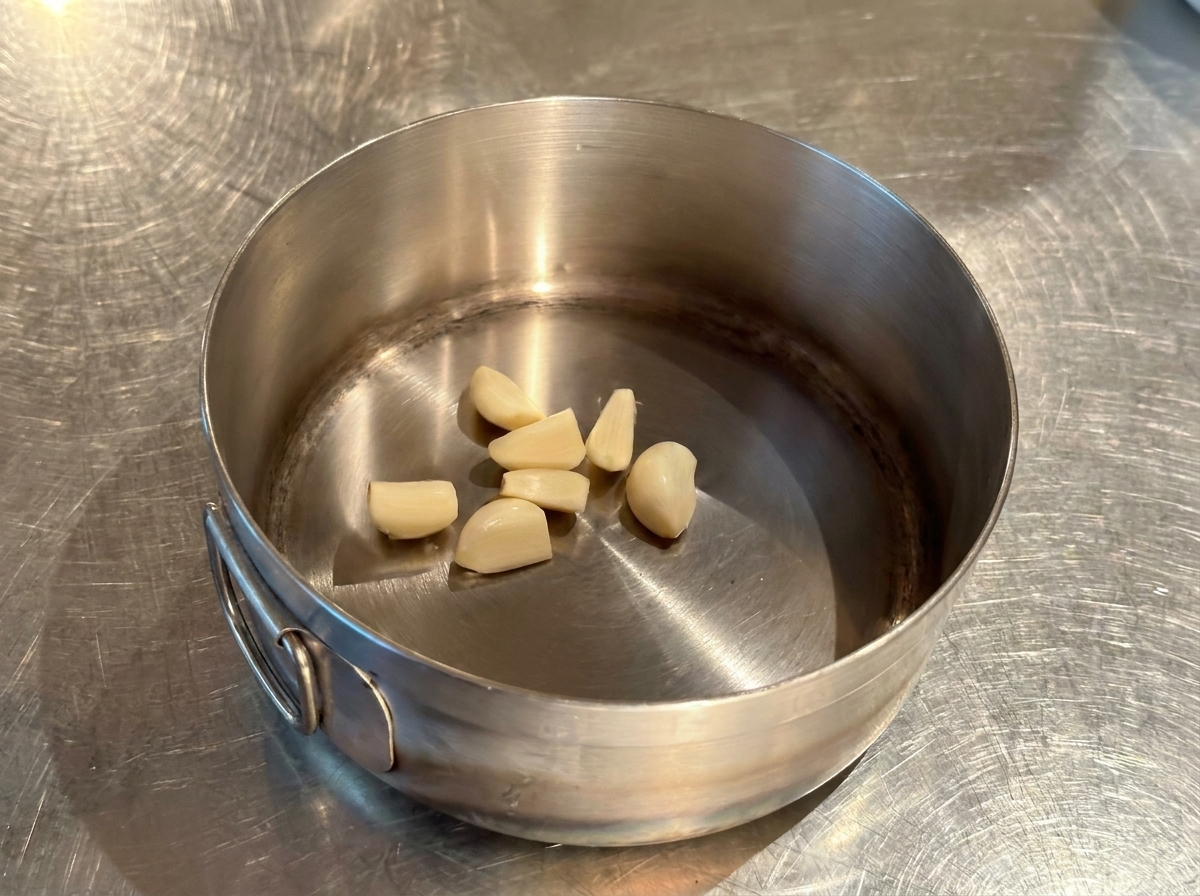 Varios dientes de ajo pelados en el fondo de una olla pequeña de acero inoxidable.