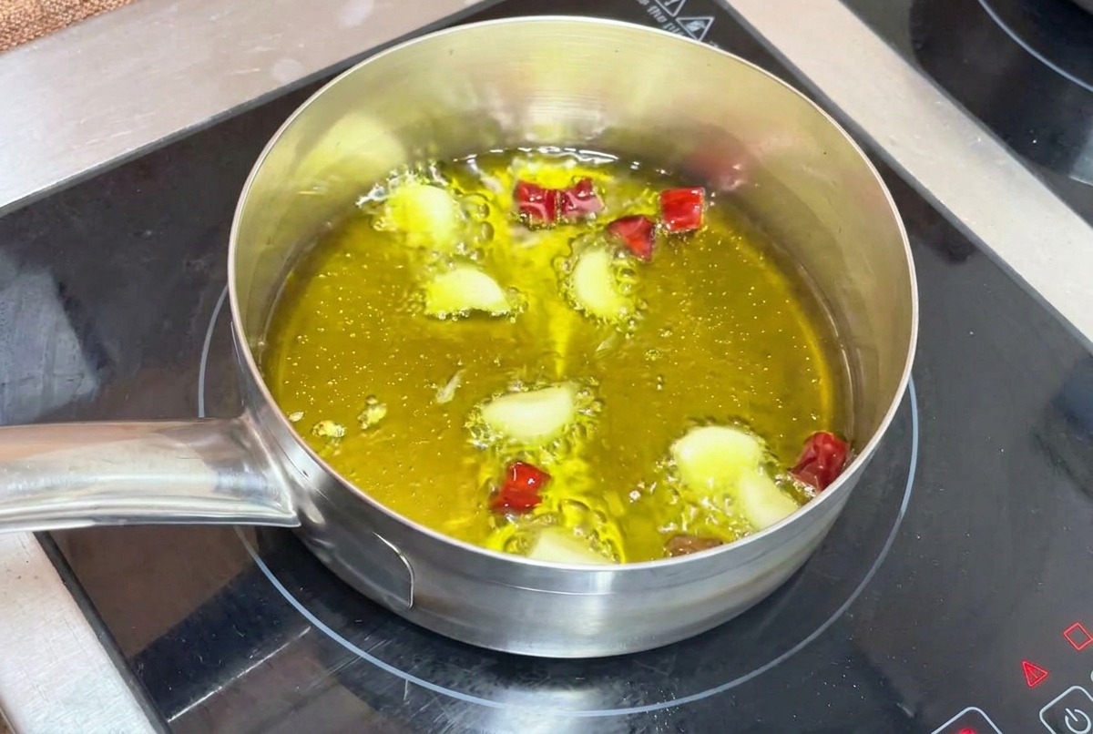 Ajos y chiles picados friéndose suavemente en aceite de oliva burbujeante en una olla pequeña.