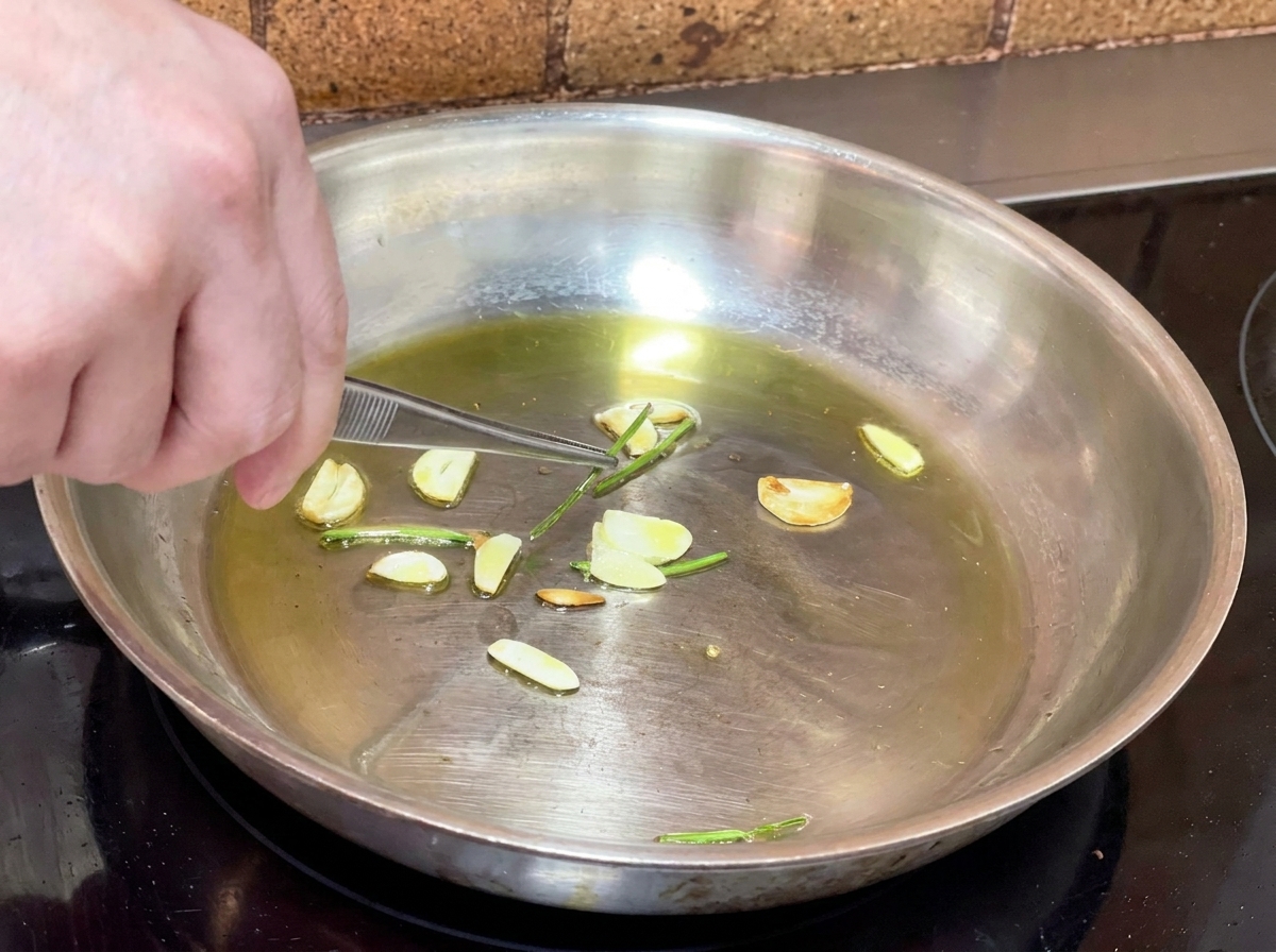 Pinzas metálicas retirando los tallos de perejil de la sartén con aceite infusionado.
