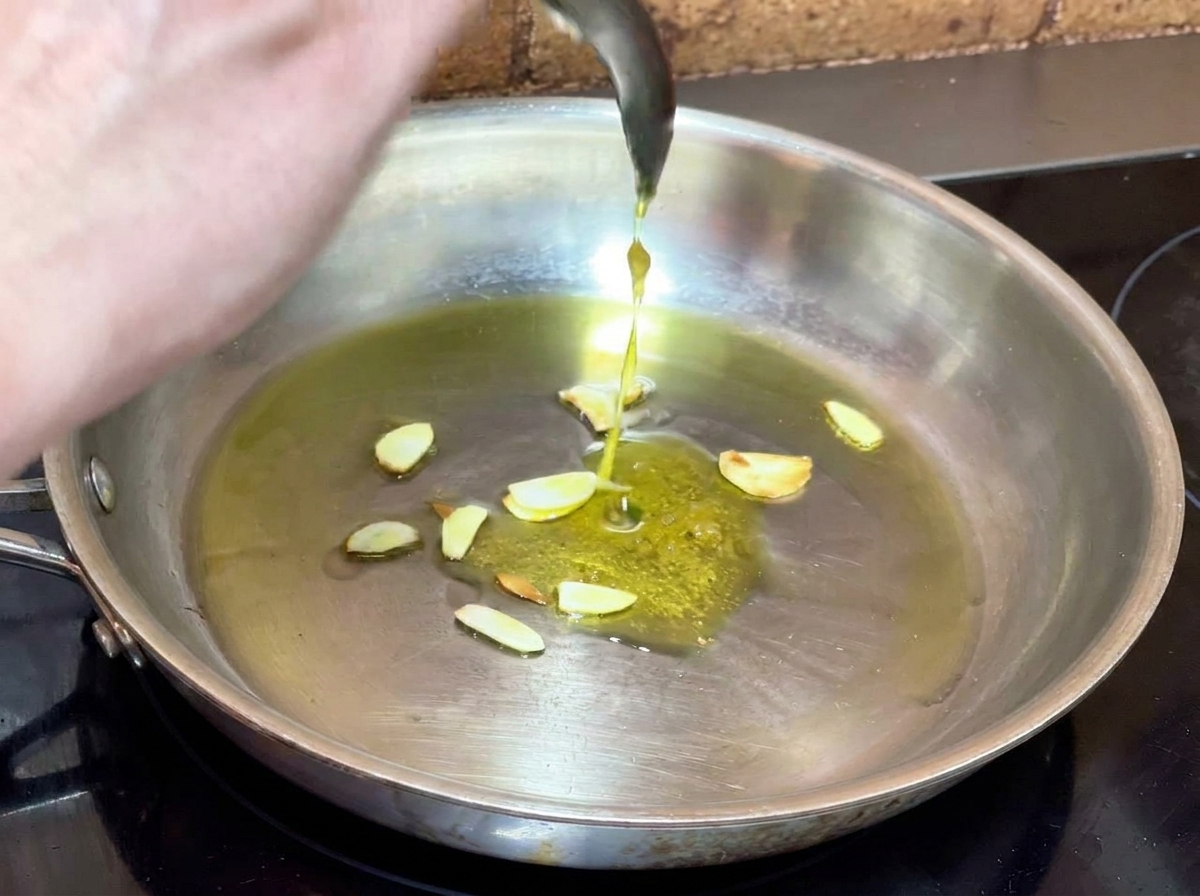 Echando la pasta de ajo preparada en una sartén con aceite infusionado y ajo laminado.