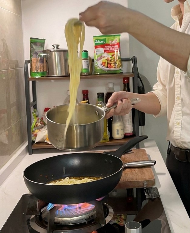 Espaguetis cocidos siendo levantados de la olla con pinzas para añadirlos a una sartén caliente con aceite sazonado.