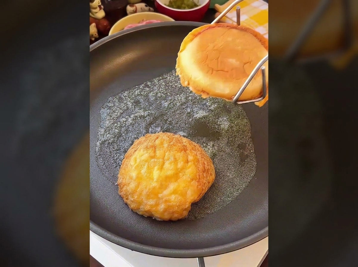 Dos mitades de pan de hamburguesa tostándose boca abajo en una sartén con mantequilla hasta estar doradas.