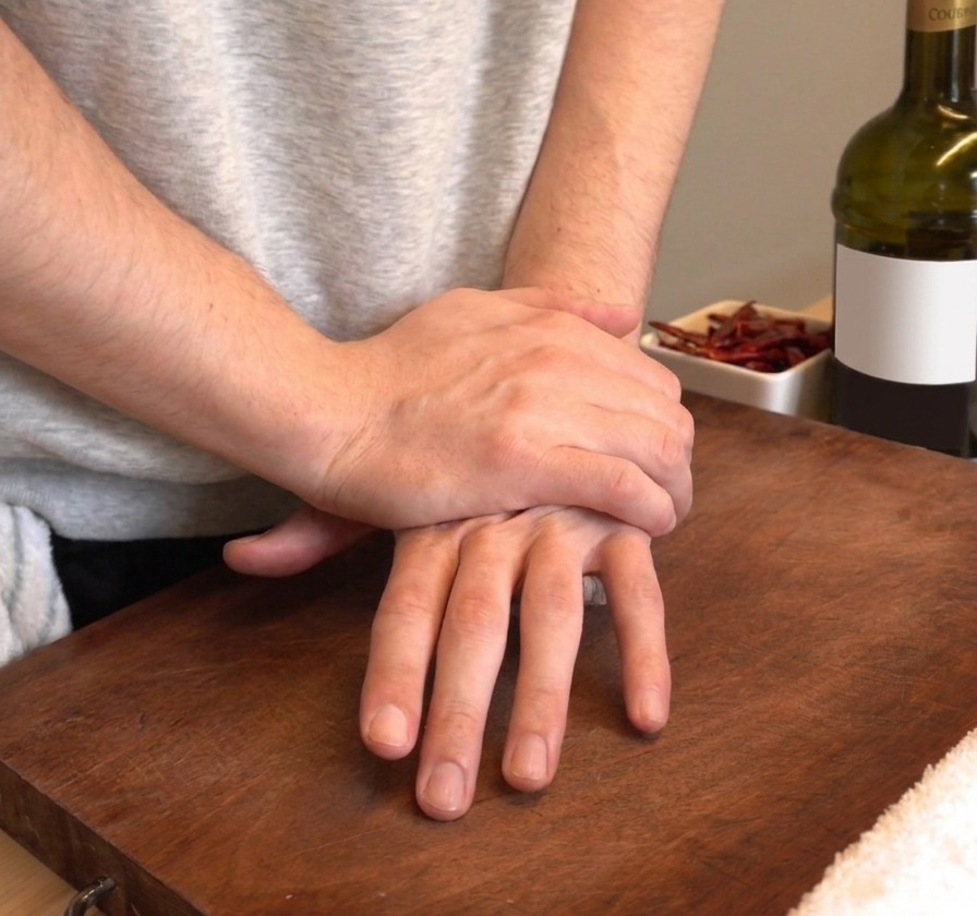 Manos presionando con firmeza para aplastar dientes de ajo frescos sobre una tabla de cortar de madera.