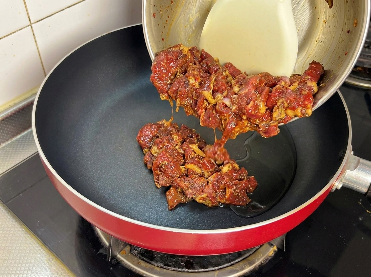 Ternera marinada vertiéndose en una sartén muy caliente con aceite.