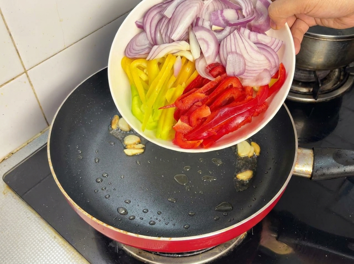 Cebolla morada y pimientos troceados siendo añadidos a una sartén caliente con aceite.