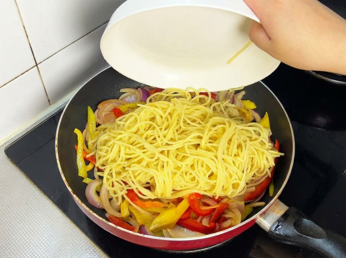 Láminas de carne cocinada volviendo a la sartén con espaguetis y verduras.