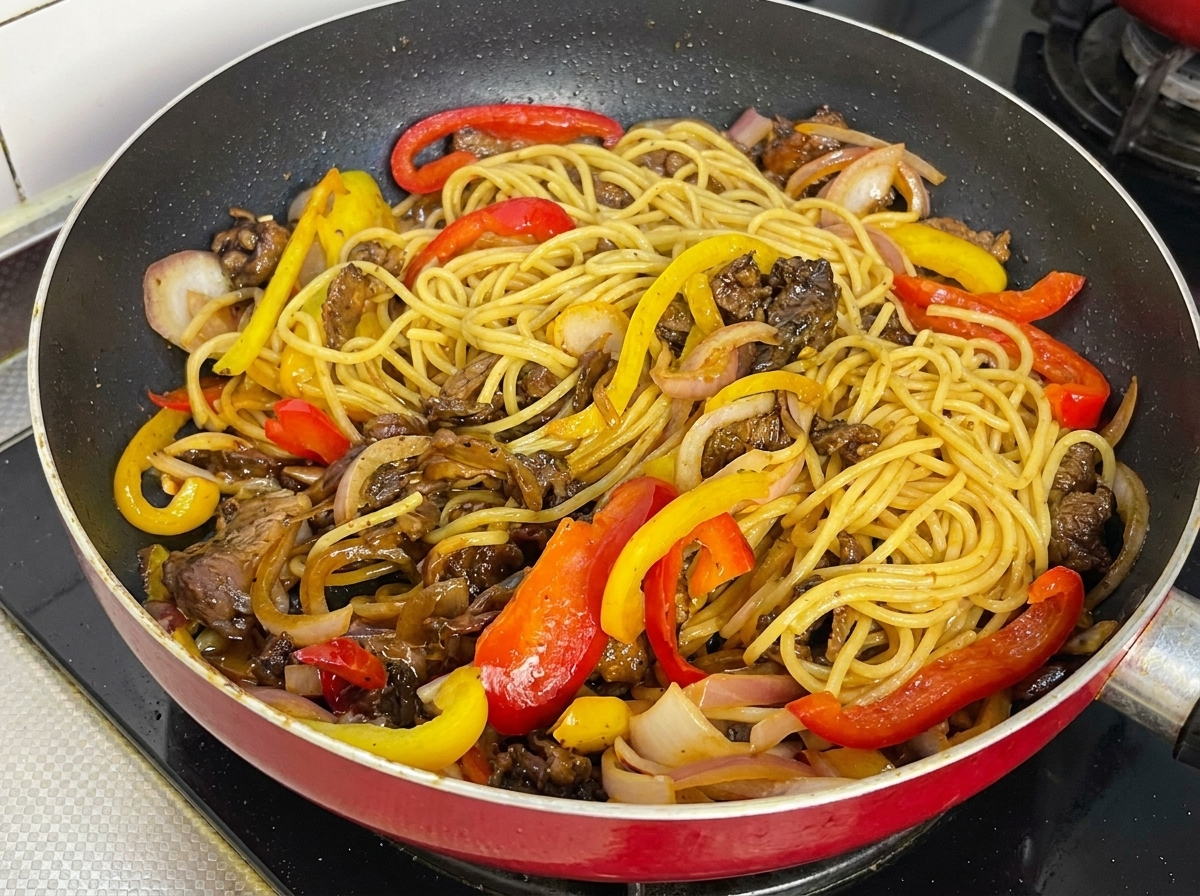 Espaguetis, ternera y pimientos mezclados y cubiertos por la salsa brillante en la sartén.