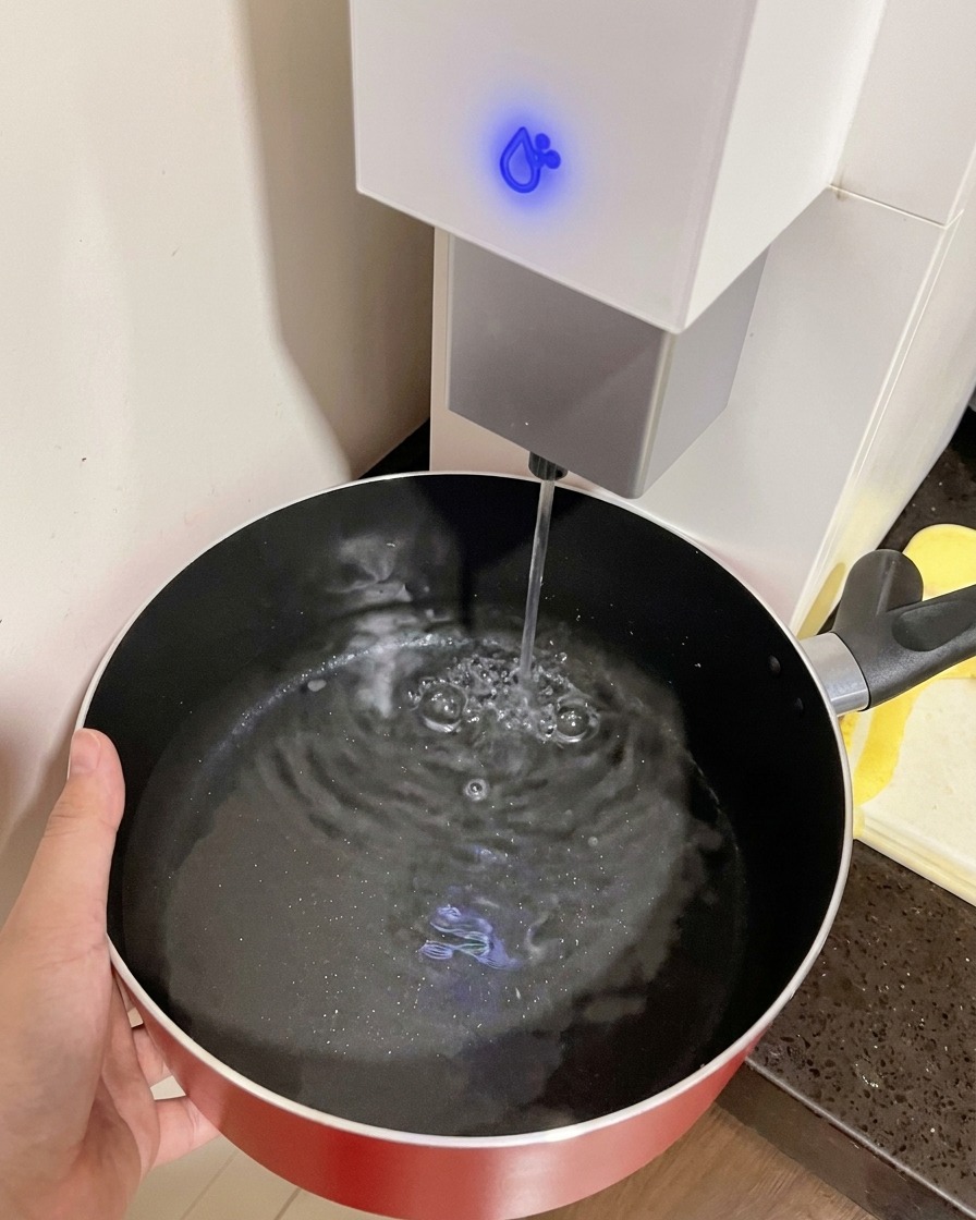 Una mano sosteniendo una olla roja mientras se llena con agua de un dispensador.
