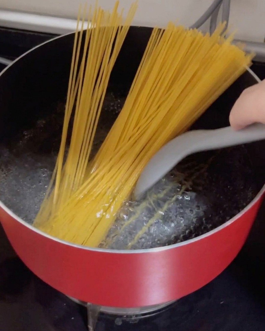Espaguetis secos siendo introducidos en una olla roja con agua hirviendo vigorosamente.